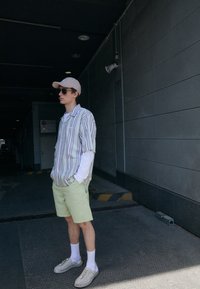 Camisa de manga corta a rayas en colores pastel, combinada con pantalones cortos de cuadros en verde claro. Los accesorios incluyen una gorra beige y gafas de sol. Calzado casual.