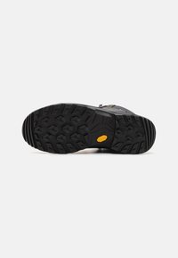 Semelle de chaussure de randonnée noire avec des crampons profonds multidirectionnels et un petit logo jaune Vibram près du centre.