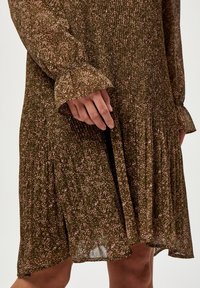 Vihreä kukkamekko vaaleanpunaisilla pisteillä, teksturoitu kangas, liehuvat hihat ja kerrostettu hameosa. Kevyt ja valuva muotoilu.