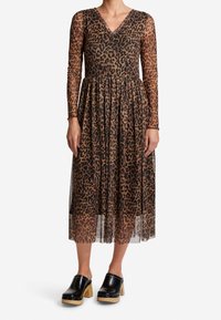 Musta muninta mekko, jossa on pitkät läpinäkyvät hihat, V-kaula-aukko, kootut vyötärö ja virtaava hame. Yhdistetty mustiin puukengiin, joissa on puukorot.