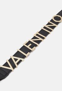 Černý kožený pásek s kovovými písmeny ve zlaté barvě, která tvoří slovo "VALENTINO," s hladkou texturou a elegantním, strukturovaným designem.