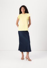 Gul kortermet topp med rynkede skuldre, kombinert med en marineblå satin maxi-skjørt. Lycra sandalett med tan farge avslutter antrekket.