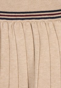 Beige pleated knit skirt with a ribbed waistband featuring navy and burgundy stripes, textured fabric, and uniform pleats throughout.