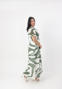 Robe longue à motif présentant des designs ondulés verts et blancs, fabriquée en tissu léger. Comprend des manches courtes et une taille cintrée.