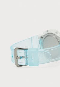 Bracelet de montre bleu transparent avec une boucle en métal argenté ; présente une texture lisse et une forme arrondie, reliant à un cadran de montre blanc.