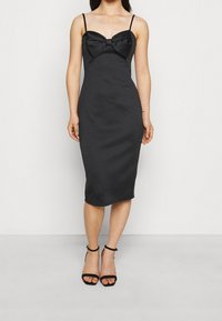 Svart tajt midiklänning med tunna band, med en strukturerad rosettdetalj vid bysten och ett slätt, texturerat tyg.