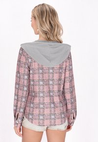 Camicia a quadri rosa e grigia con cappuccio grigio testurizzato, maniche lunghe e polsini con bottoni. Il motivo a scacchi distintivo aggiunge interesse visivo.