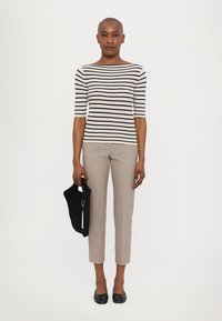Haut en tricot rayé crème avec des rayures marines, associé à un pantalon beige bien ajusté. Tient un sac en tricot noir et porte des ballerines noires.
