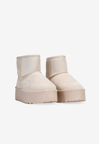 Botas beige hasta el tobillo hechas de ante, con una textura suave, suela plana y un diseño sencillo y redondeado sin cierres visibles.