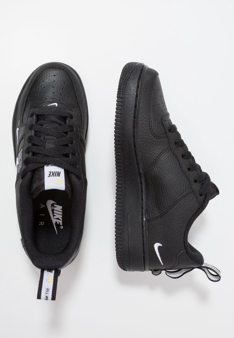 Černé tenisky Nike Air s texturovaným koženým povrchem, šněrovacím designem, perforovanou špičkou a bílými logovými akcenty na stranách a jazyku.