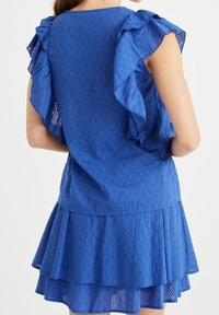 Niebieska sukienka w paski z falbaniastymi rękawami i warstwowym krojem spódnicy. Tkanina ma lekką fakturę i zwiewny krój.