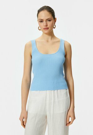 Top sin mangas de canalé azul claro con escote cuadrado y tirantes anchos, combinado con pantalones de pierna ancha blancos y texturizados, creando un look en capas.