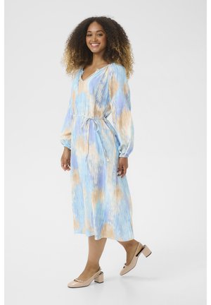 Vestito lungo azzurro fluido con motivo astratto marrone e crema; polsini elasticizzati, scollatura a V e vita regolabile con lacci. Abbinato a scarpe beige con tacco blocco.