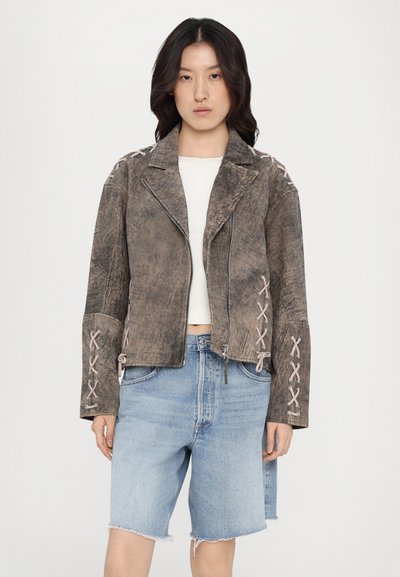 Brun konstläderbikerjacka med texturerad yta, dragkedjeslutning och snörade detaljer på ärmarna. Matchad med ljusa denimshorts.