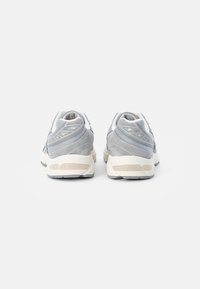Zapatillas deportivas grises con parte superior de malla texturizada y ante, que cuentan con una entresuela blanca, un collar acolchado y detalles reflectantes. Vista trasera mostrada.