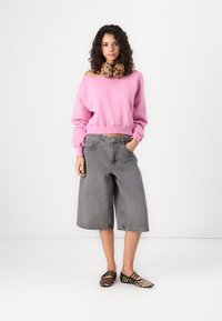 Maglione rosa off-shoulder, pantaloni shorts in denim grigi a ginocchio, e scarpe leopardate nere e beige. Il tessuto sembra morbido e casual.