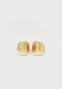 Gold metallic slip-on shoes with a smooth texture, white rubber soles, and embossed brand logo on the heel. Simple design, no laces.