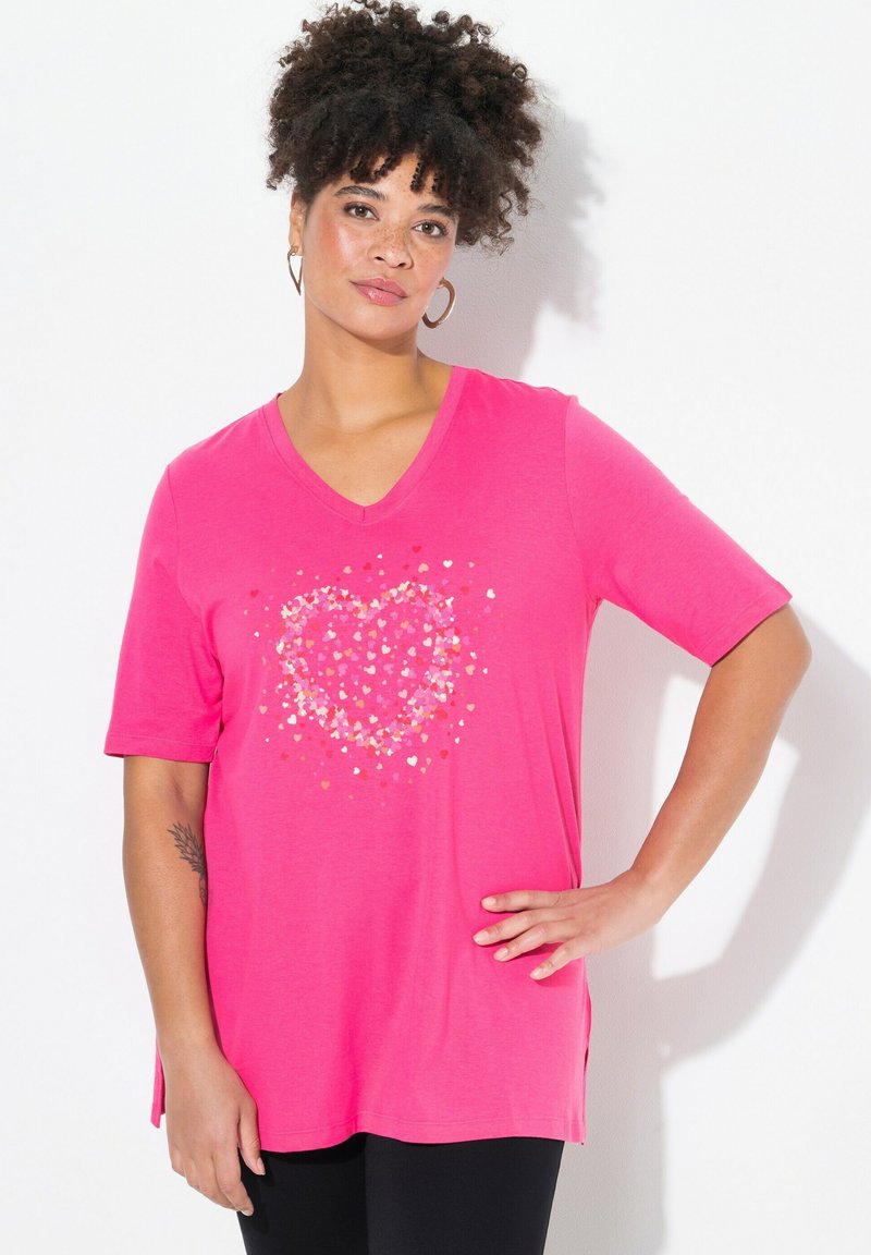 Camiseta rosa de cuello en V con mangas cortas que presenta un diseño de corazón hecho de formas brillantes y multicolores. Tela suave y ligera con aberturas laterales.