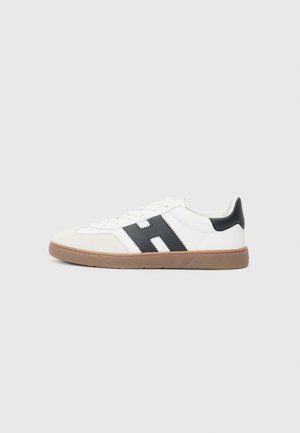 White sneakers with black accents, featuring a textured surface, rounded toe, lace closure, and a light brown rubber sole.
