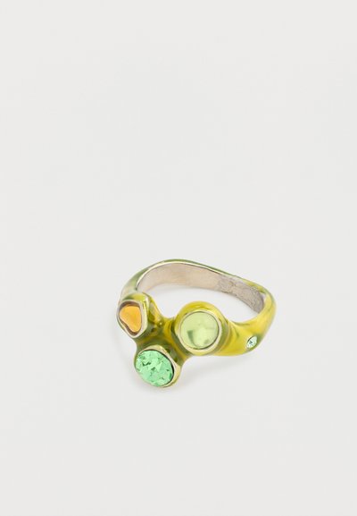 Bague verte et jaune avec trois pierres gemmes circulaires : une verte transparente, une verte claire et une ambre, serties dans un anneau lisse et texturé.