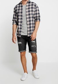 Ruudullinen flanellipaita navy, valkoista ja beigeä, harmaa t-paita, mustat farkkushortsit revityillä yksityiskohdilla ja valkoiset lenkkarit. Rentoa vaatetusta.