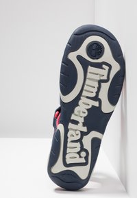 Navy and gray outsole features a prominent white "Timberland" logo. Non-marking rubber with textured surface and grip patterns.