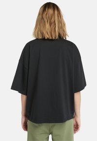 Černé oversized bavlněné tričko s krátkými rukávy, volný střih a čistým zakončením. Pairs s světle zelenými kalhotami.