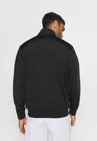 Chaqueta atlética negra con un acabado suave, cuello alto y puños acanalados, con un corte relajado y un diseño simple y sin adornos.