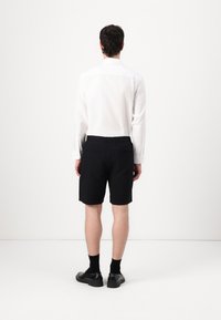Black shorts with a flat-front design, medium length, and rear pockets, paired with a white long-sleeve shirt and black shoes.