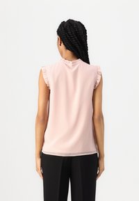 Haut sans manches rose clair avec accents froncés aux épaules, tissu lisse, encolure ronde, présentant une coupe décontractée et une légère brillance.