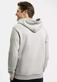 Szara bluza z kapturem o miękkiej fakturze, z luźnym krojem, sznurkiem w kapturze oraz prążkowanymi mankietami przy nadgarstkach i u dołu.