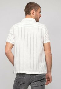 Chemise pour homme à manches courtes en tissu blanc texturé avec de fines rayures verticales noires, dotée d'un col classique et d'un ourlet droit.