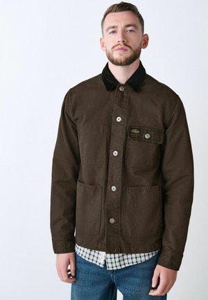 Brown cotton jacket with a corduroy collar, front snap buttons, two chest pockets, and a textured finish over a plaid shirt.