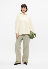 Κρέμα φούτερ με γραφικό σχέδιο, άνετη εφαρμογή; ανοιχτό πράσινο παντελόνι σε φαρδιά γραμμή; πράσινο τσάντα με κέντημα, μαύρα παπούτσια με λεπτομέρειες.