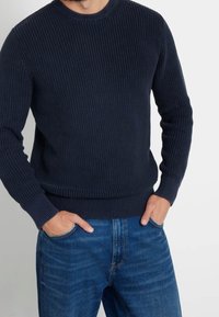 Marinblå ribbad stickad tröja med långa ärmar och rundad halsringning, ihopparad med ljusblå denimjeans. Tröjan har ett texturerat mönster.