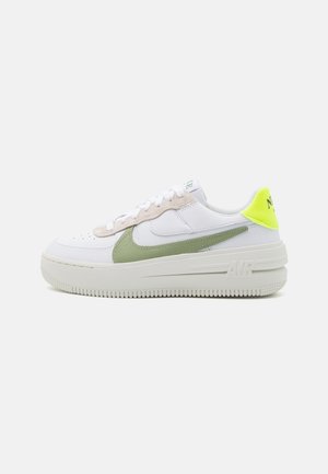 Baskets basses blanches avec un swoosh Nike vert clair, languette de talon jaune néon, détails en daim beige et semelle épaisse en caoutchouc blanc marquée "AIR".