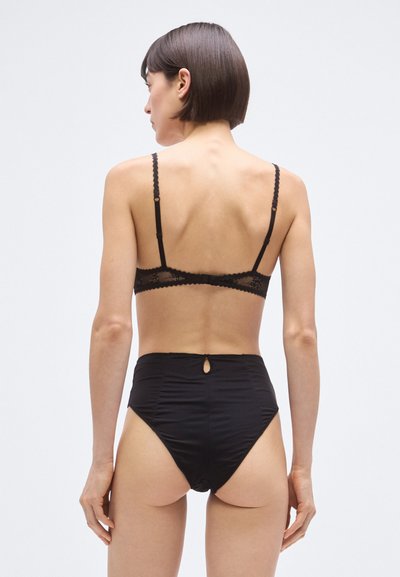 Melns apakšveļas komplekts ar mežģīņu apdari braletē un augstās jostasvietas biksītēm ar atslēgas caurumu aizmugurē.