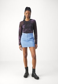 Un haut à manches longues en tie-dye violet associé à une mini-jupe en denim bleu clair, rehaussé par des bottines noires et un design épuré.