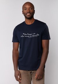 Marineblauwe katoenen t-shirt met op de voorkant handgeschreven witte tekst, een ronde hals en korte mouwen. Glad textuur.