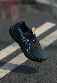 Baskets de sport bleues au design élégant, tige en synthétique, surface texturée, accents orange et lacets noirs ; semelle légère avec traction.