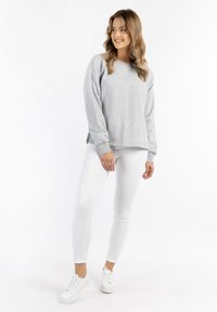 Felpa grigia a collo rotondo con maniche lunghe, texture morbida e polsini a coste, abbinata a jeans skinny bianchi e sneakers bianche.