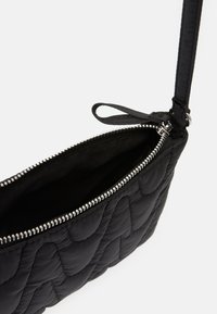 Černá prošívaná kabelka hladké textury, se zipovým uzávěrem a štíhlým popruhem. Interiér je podšívkovaný látkou a má jednoduchý siluet.