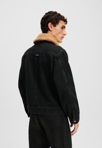 Chaqueta de mezclilla negra con un cuello de pelo sintético color beige. Presenta un corte relajado, costuras visibles y puños abotonados.