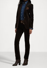 Brązowa marynarka ze sztruksu na niebieskiej dżinsowej koszuli, zestawiona z brązowymi spodniami ze sztruksu i botkami za kostkę. Marynarka posiada charakterystyczny detal kieszeni.