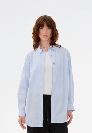 Lyseblå skjorte med knaplukning, stribet mønster, lange ærmer og afslappet pasform. Har sølvknapdetaljer og klassisk krave.