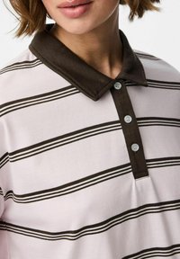 Triibuline polo särk heleses roosas toonis, tumepruun krae. Omab kolme nuppi ja õhukesi horisontaalseid triibusid lihtsa disaini jaoks.