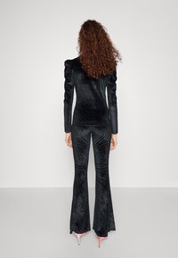 Completo in velluto nero con motivo a righe verticali; giacca aderente con spalle imbottite e pantaloni svasati; completato con scarpe rosa con tacco.