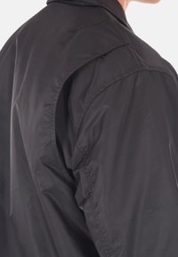 Giacca leggera nera con una texture morbida, caratterizzata da colletto alto e dettagli cuciti sulle spalle, vista di lato.