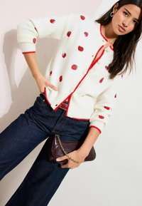 Valge kootud kardigan punaste maasikapatroonide, punase ääre ja nööpidega. Kandmiseks koos tumedate teksade ja burgundi värvi kettaga klanitud õlakotiga.