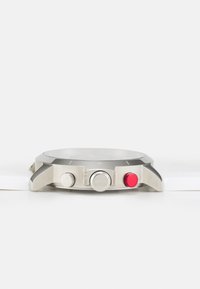 Silver stainless steel watch featuring a round case, two buttons, one red and one silver, and a white band. Minimalist design with clear dial.